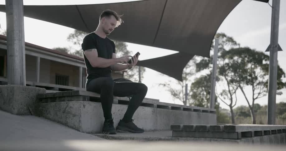 A man uses his phone while sitting on the concrete