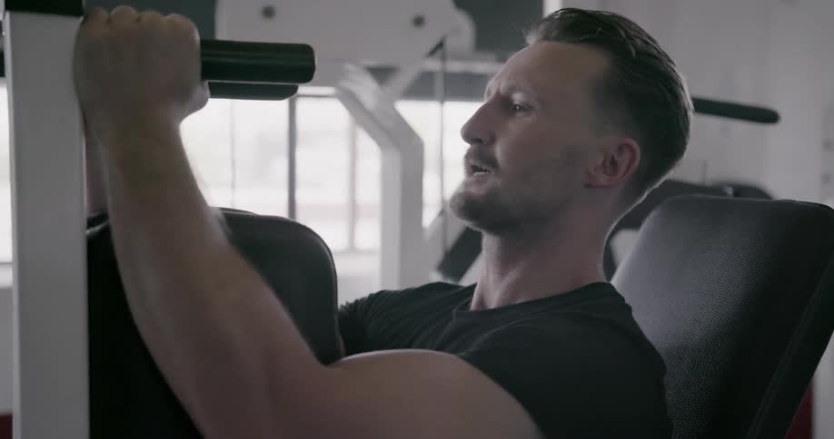 A man is working out on a pec machine in a gym during the day
