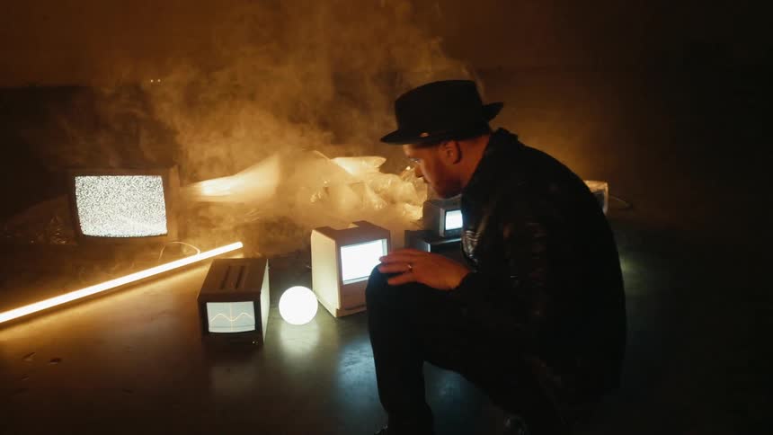 Man crouches next to tvs on the floor of a smoky room