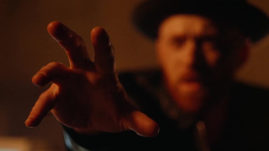 A man crouches with his arm outstretched in a dark room