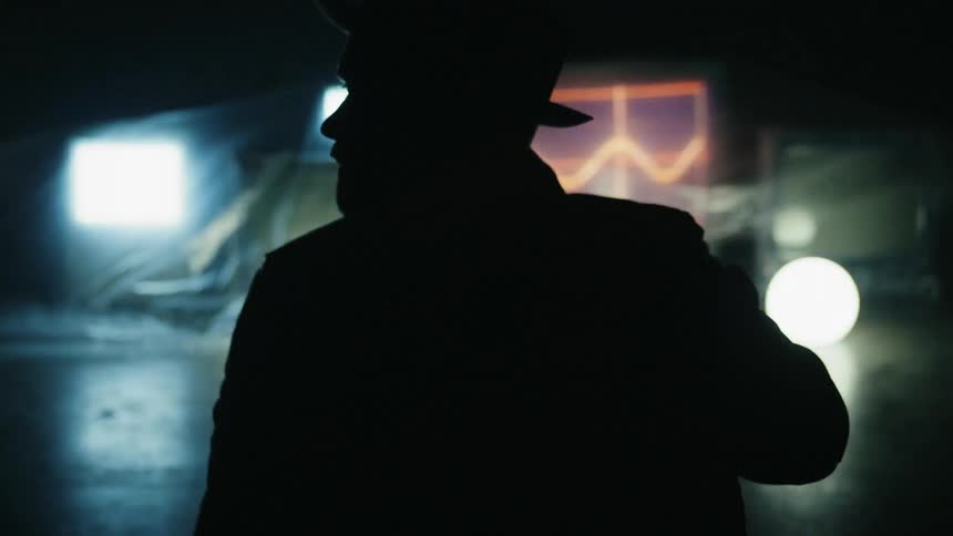 Man sits near tvs on the floor of a smoky room with flashing lights
