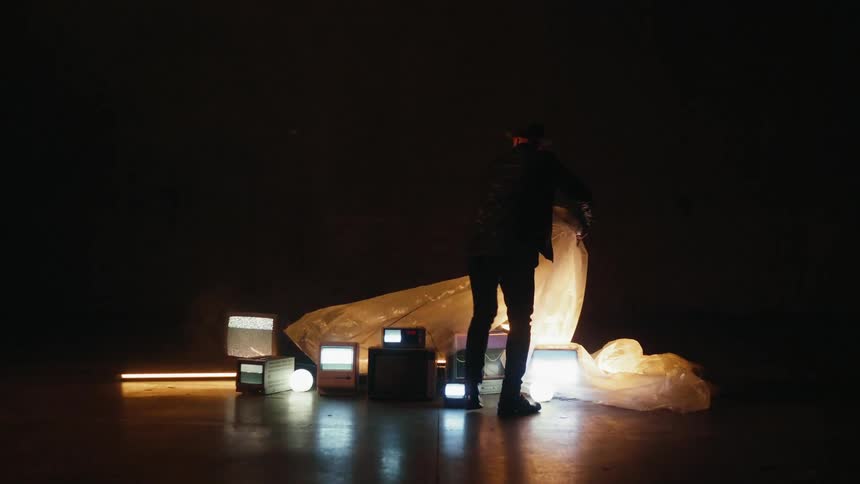 A man is pulling a plastic sheet of a collection of monitors on the floor in a dark room