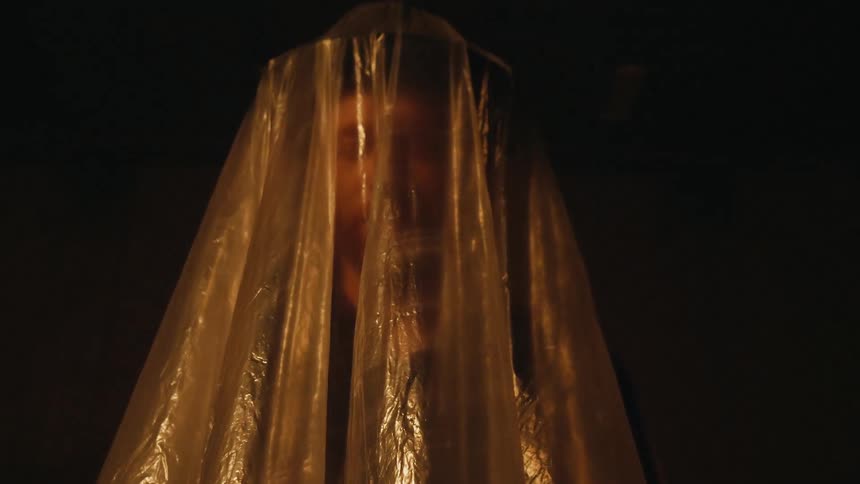 A plastic sheet covers a man's head in the dark
