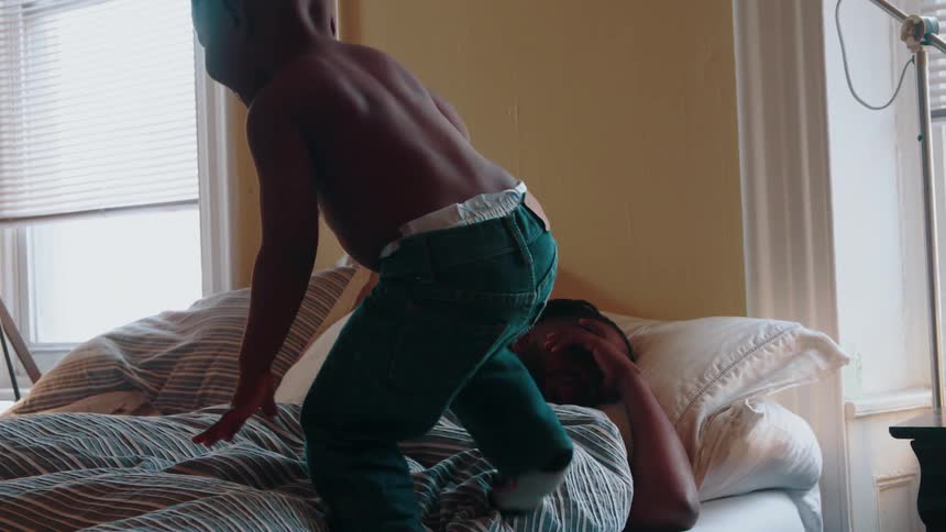 A boy is climbing onto his father's bed and jumping on him in the morning
