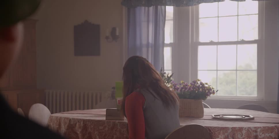 A boy wearing a helmet walks into the dining room to see his mom who is listening to the radio