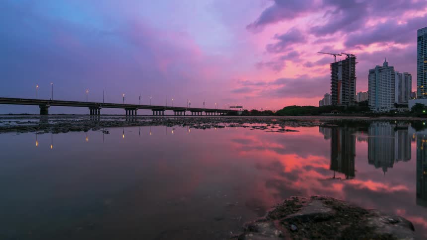 The clouds turn colors at sunset while cars go by on the bridge