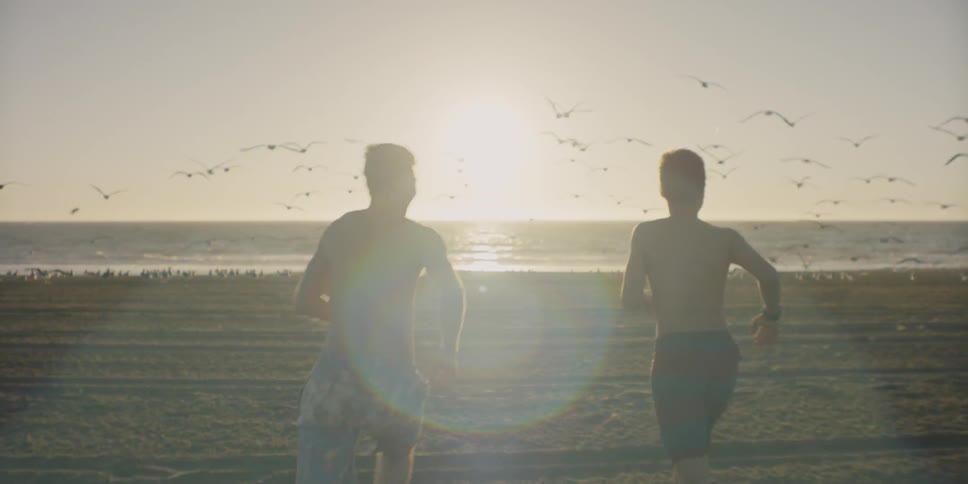 Two men run on the beach towards the water