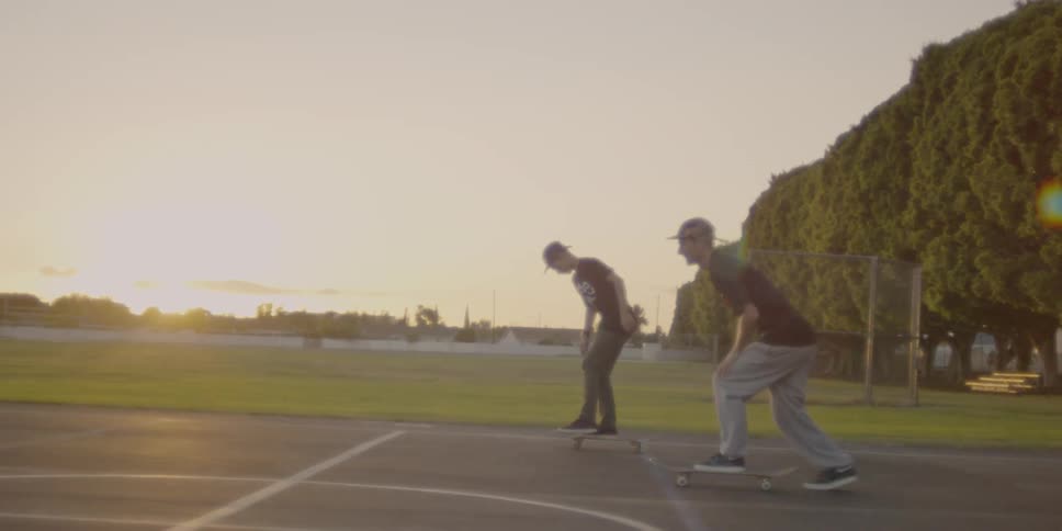 Two people ride their skateboards in the park at sunset