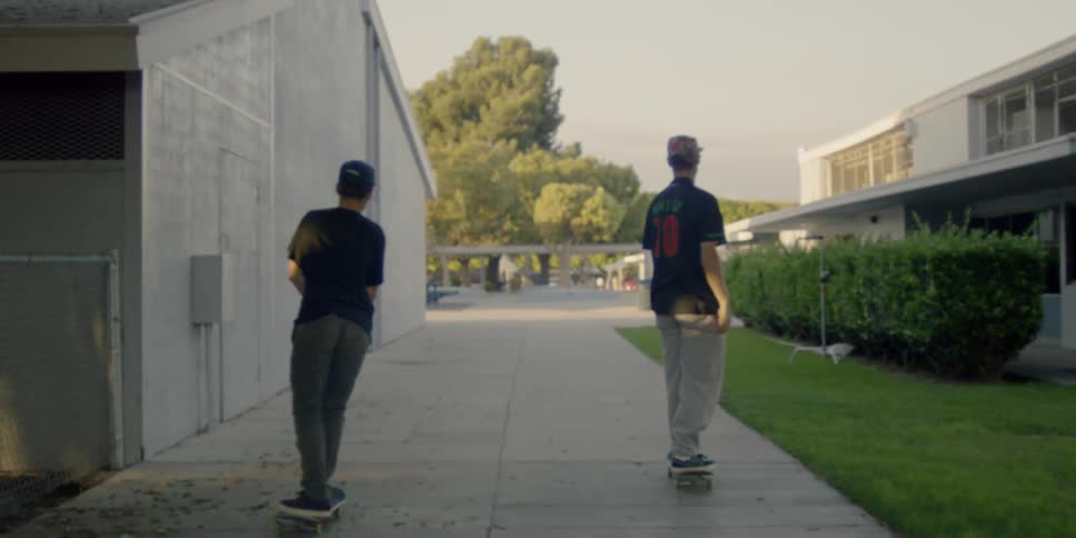 Teenagers are skateboarding on a sidewalk on school grounds during the day