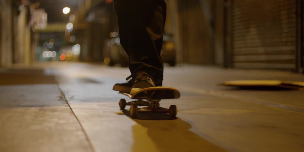 A skateboarder pushes off and rides on a city alley at night