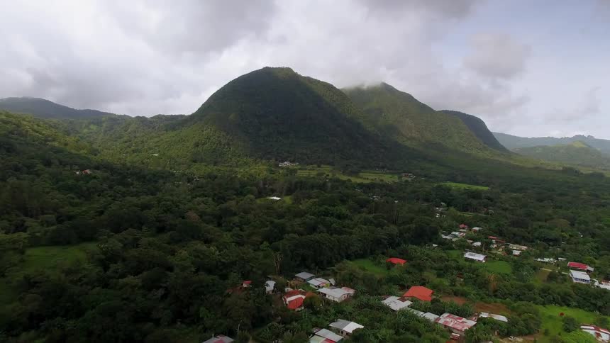 Clouds are hanging above lush green mountains and colorful roofs of a small town in Panama