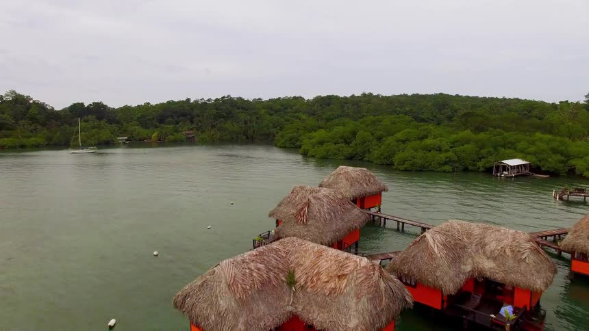 Colorful huts with thatched roofs float over a clear ocean water in Bocas del Toro