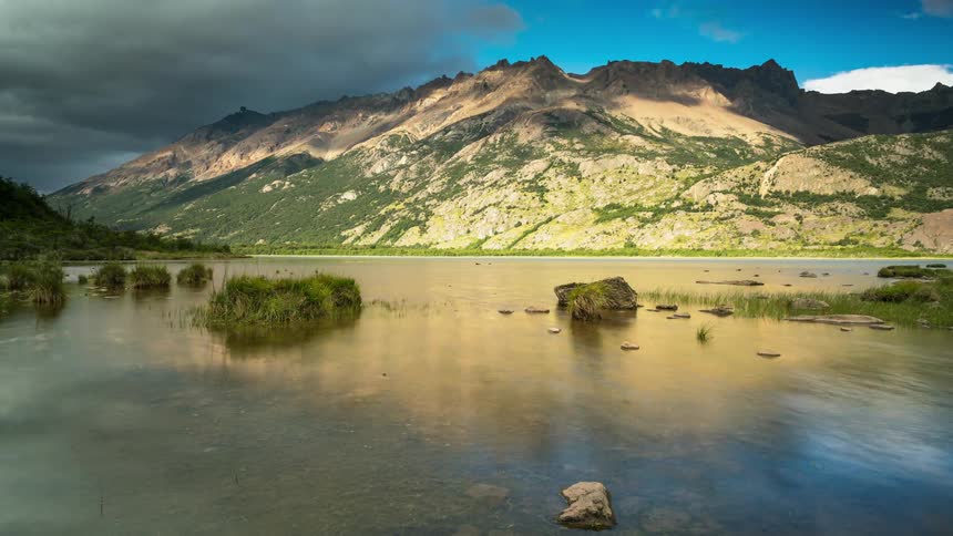 A mountain lake is reflecting passing clouds during the day