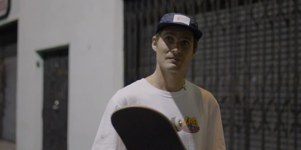 A man is standing by a building holding a skateboard
