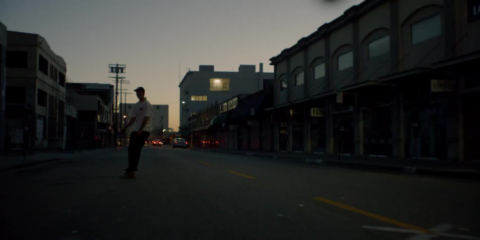 A teenager is riding a skateboard on a city street at dusk