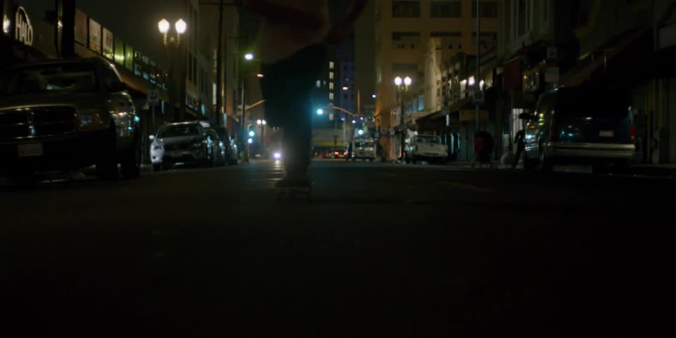 A teenager is riding a skateboard on a city street at night