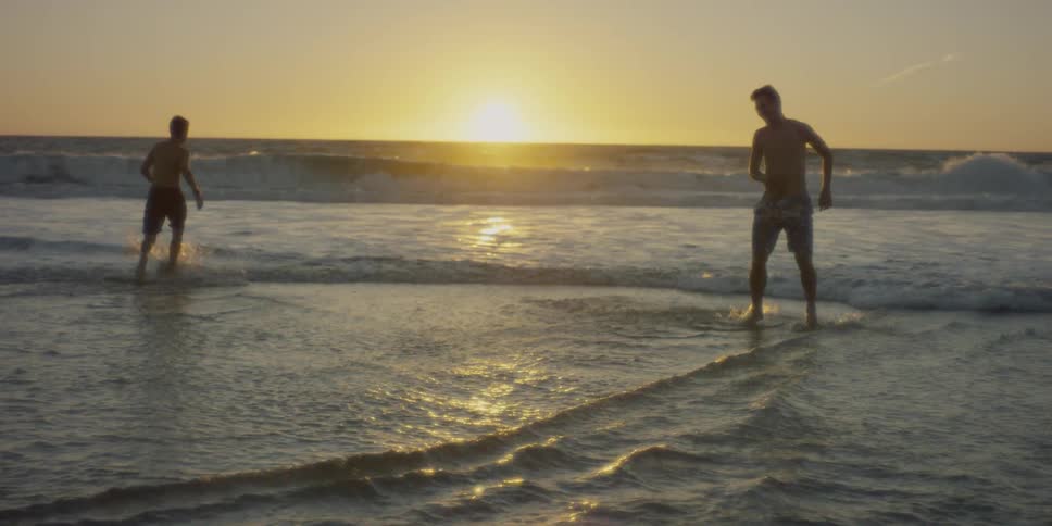Two men run in the water at sunset