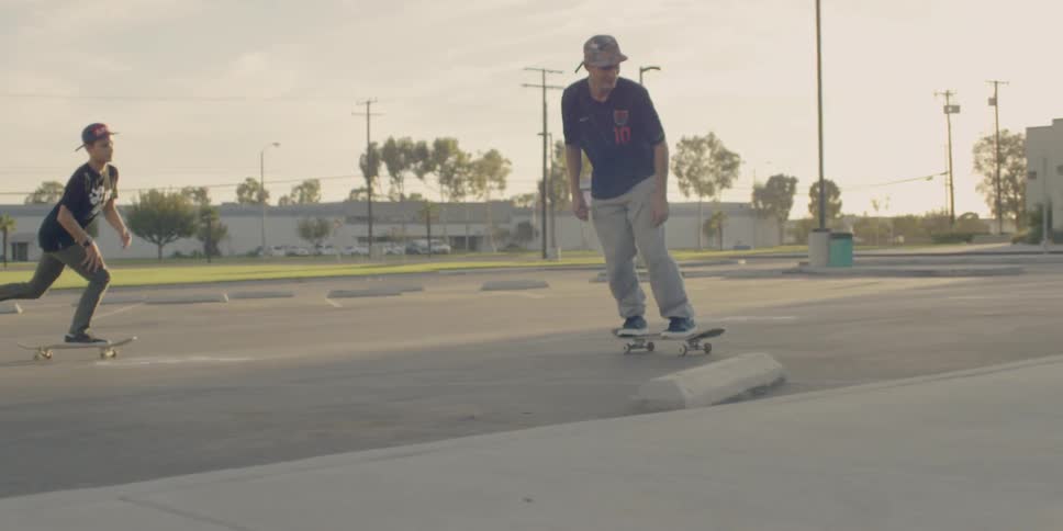 Boys skateboard through a parking lot on a sunny day