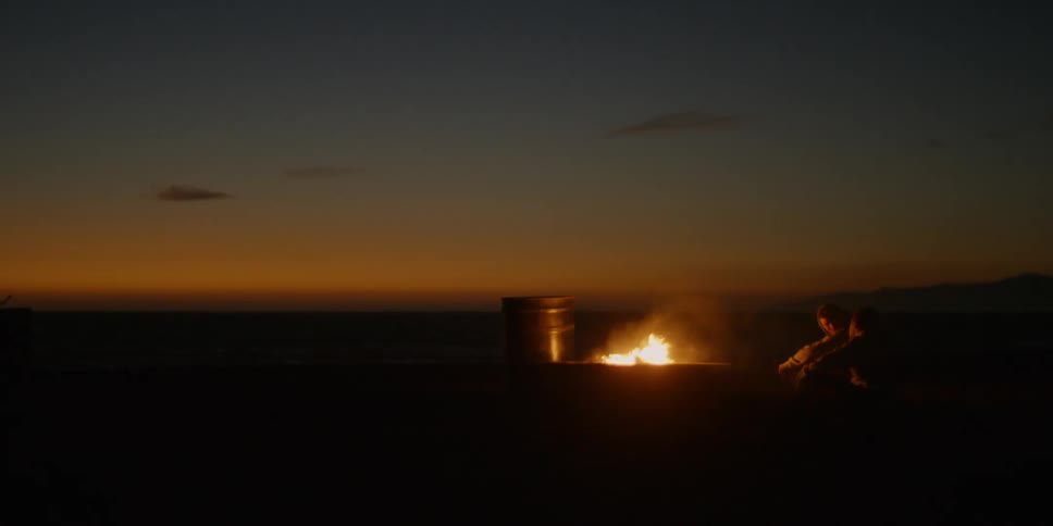 A person sits near the campfire on a windy night