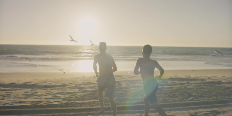 Two people run towards the water as birds fly past