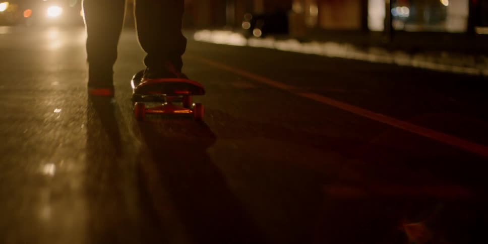 A skateboarder pushes off and rides down a street at night