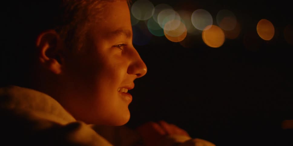 A boy talks and sits by a fire