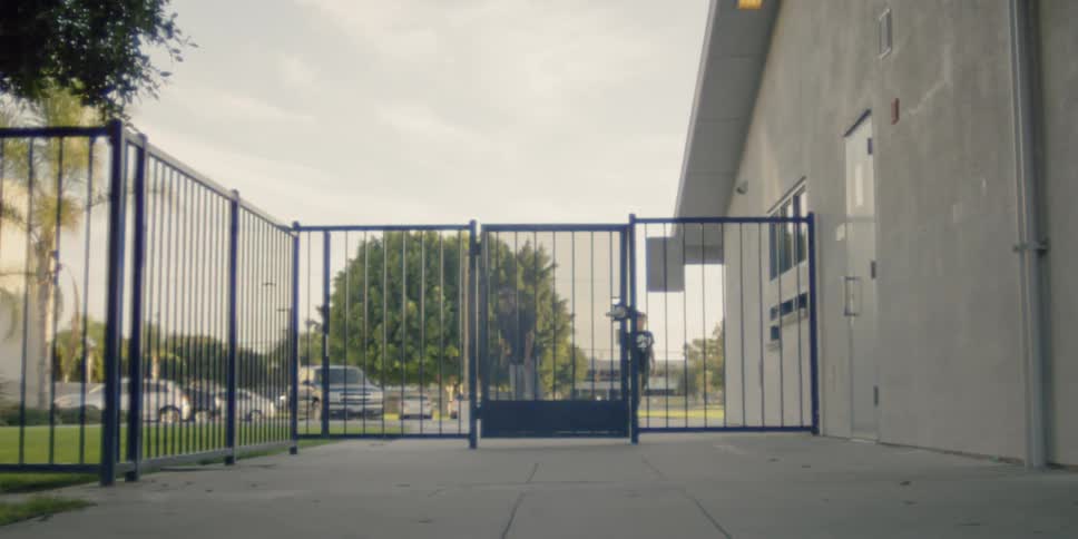 Teenagers on skateboards are approaching a gated fence in a neighborhood during daylight