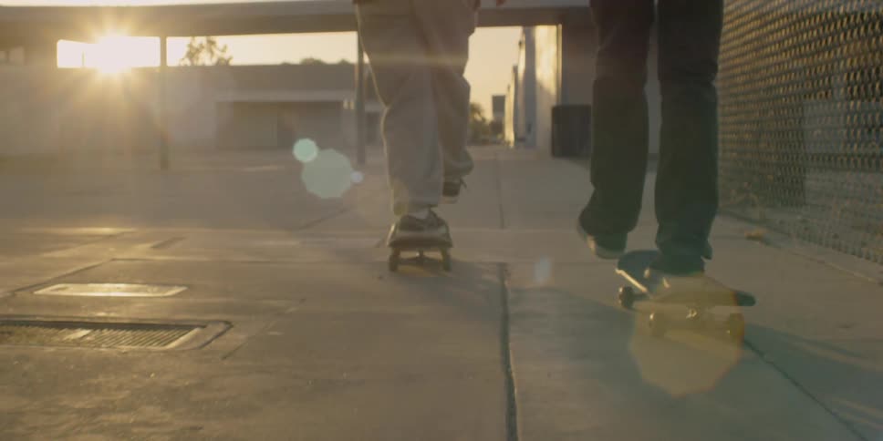 Two skateboarders are riding on a school campus during at dusk