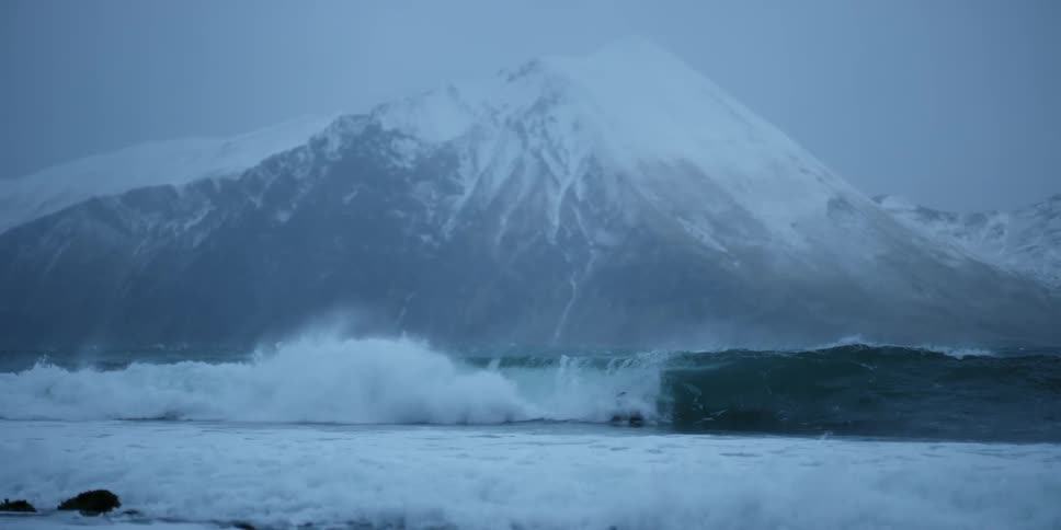 Person surfs and falls in a small wave surrounded by snowy mountains