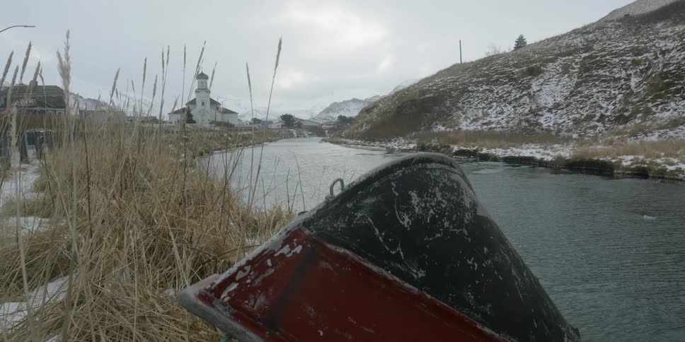 An overturned boat sits on a snowy riverbank