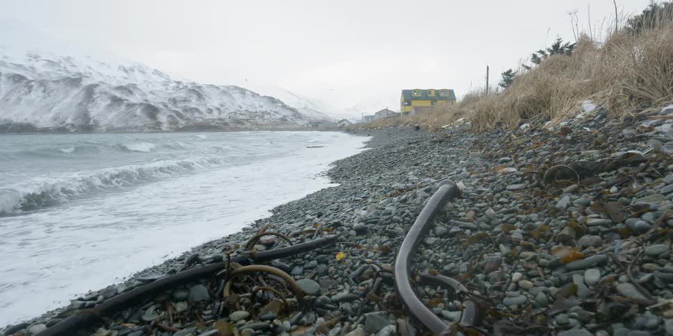 Snow falls on a rocky shore with waves splashing