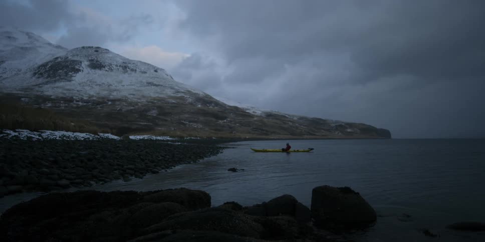 A man sits in a kayak near shore on a cloudy day