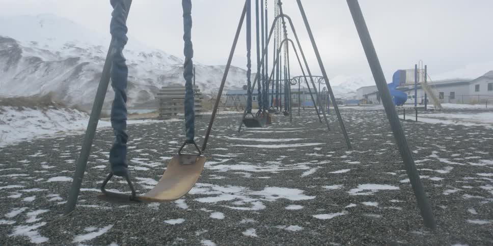 Swings on a playground sway in the wind on a snowy day