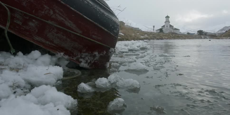 An overturned boat sits partially in the icy water