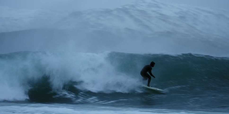 A surfer rides a tall wave in the ocean in winter
