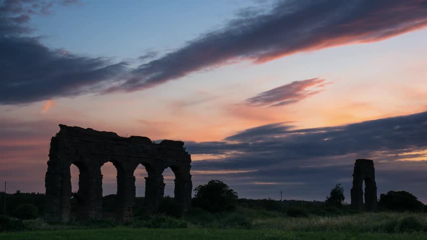 The sun sets as clouds move over ruins