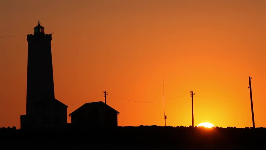 The sun sets behind a lighthouse