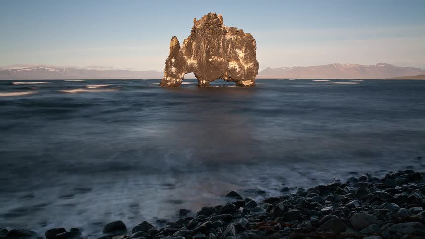 The tide is moving onto a shoreline near a rock formation throughout the day