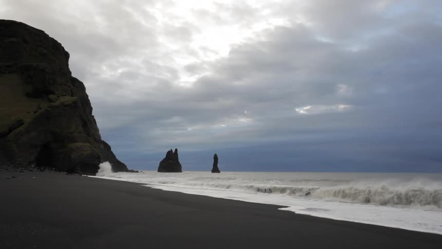 Waves are rolling onto a beach under cloudy skies