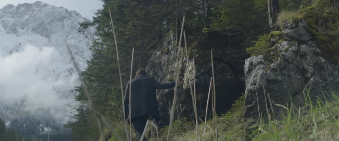A man hikes up a hill towards the forest