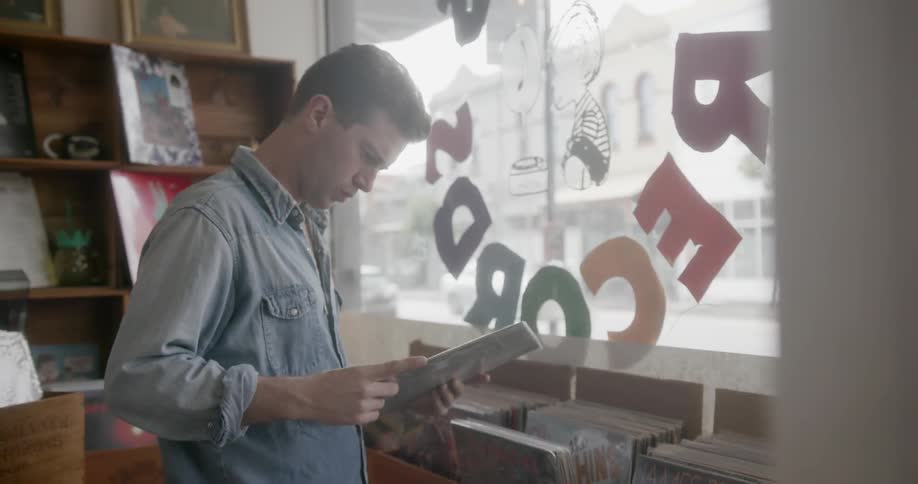 A man is dancing as he works in a record shop during the day