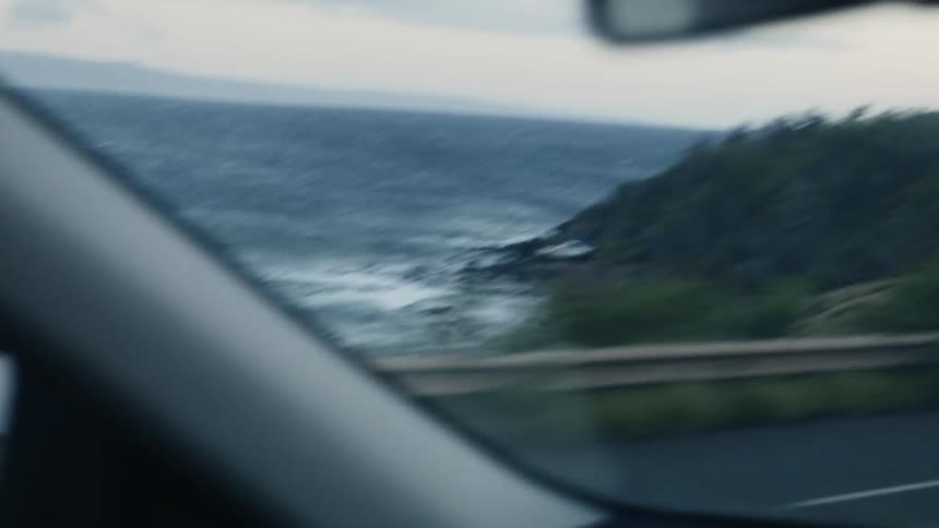 A woman is driving a vehicle on a coastal road during the day