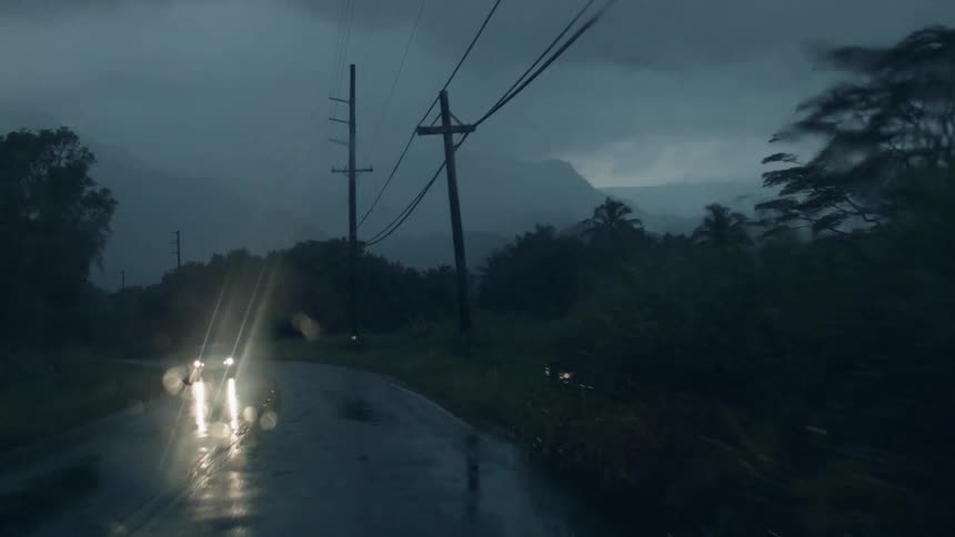 A vehicle is traveling on a country road during a rainstorm at dusk