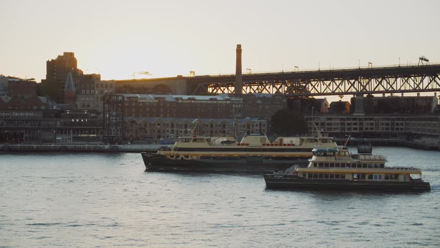 Boats are navigating a river near a city at sunset