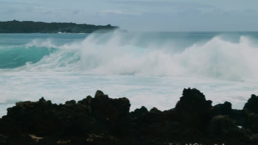 The waves crash against the rocks on a cloudy day