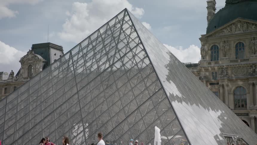 People walk by a glass pyramid structure