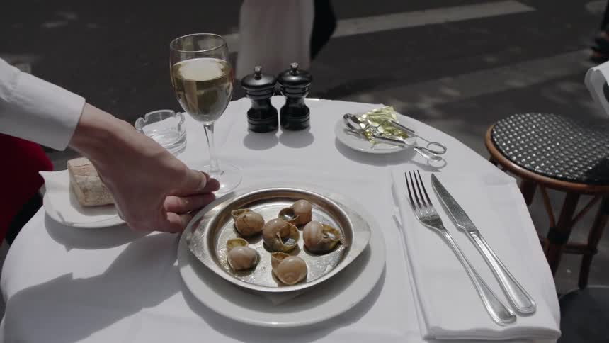 A waiter is bringing an order of escargot to a table outside during the day