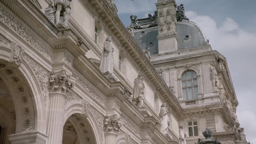 Looking at several stone sculptures above the arches of a building
