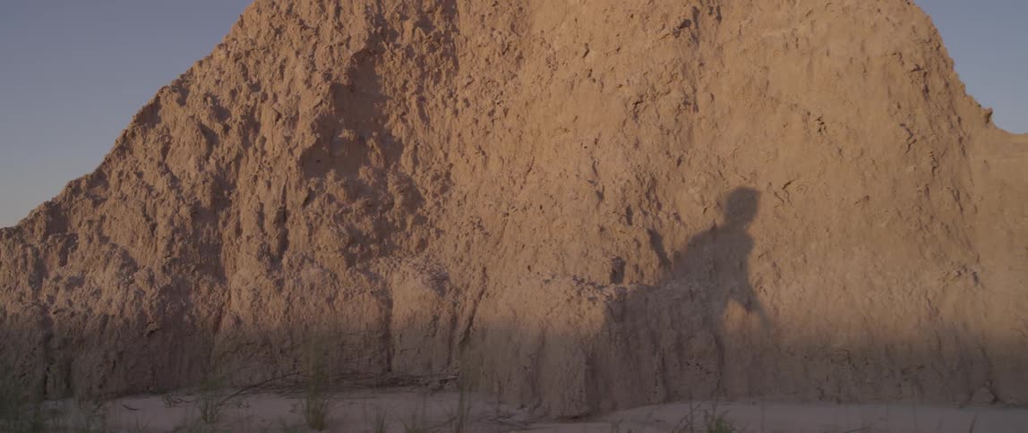 Shadow of a person walking illuminated on tall mounds of dirt