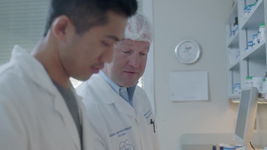 A man in a medical lab hands a paper to a colleague